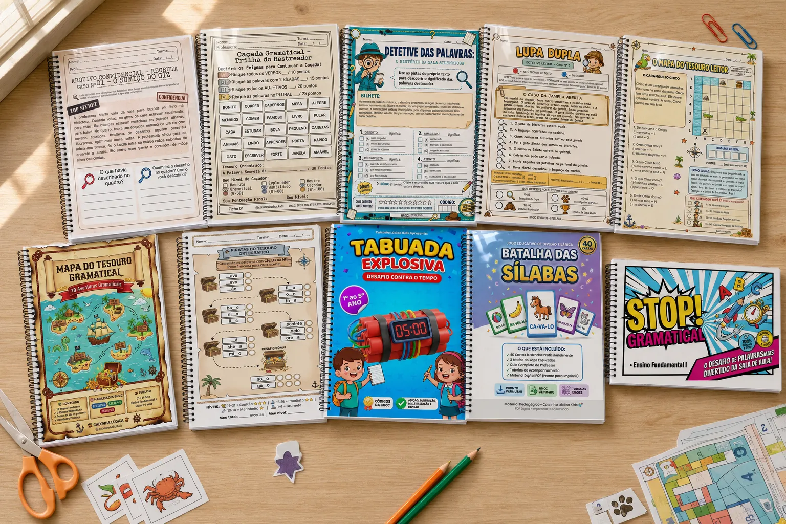 Mesa de madeira coberta pelos jogos impressos da Caixinha Lúdica: Arquivo Confidencial, Caçada Gramatical, Detetive das Palavras, Lupa Dupla, Mapa do Tesouro Leitor e Gramatical, Piratas do Tesouro Ortográfico, Tabuada Explosiva, Batalha das Sílabas e Stop Gramatical, com tesoura e lápis ao redor